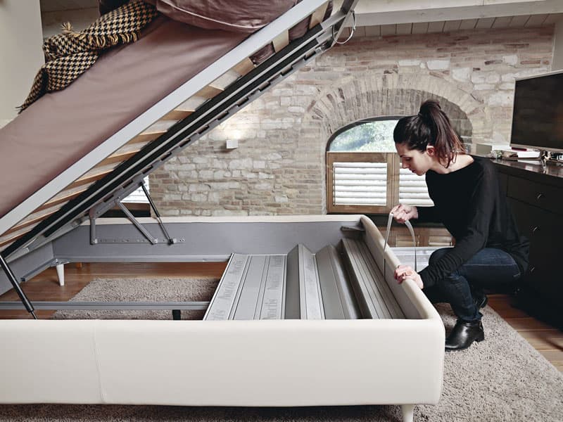 Una donna ripiega facilmente il pannello di fondo di un letto Noctis Folding Box per pulire il pavimento sottostante.